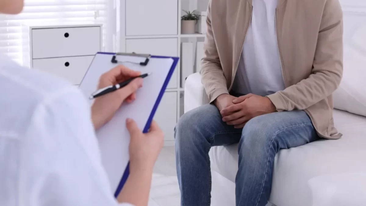 Muž sedí v ordinaci u lékaře, lékař vypl%nuje dotazník