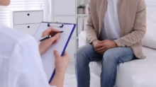 Muž sedí v ordinaci u lékaře, lékař vypl%nuje dotazník