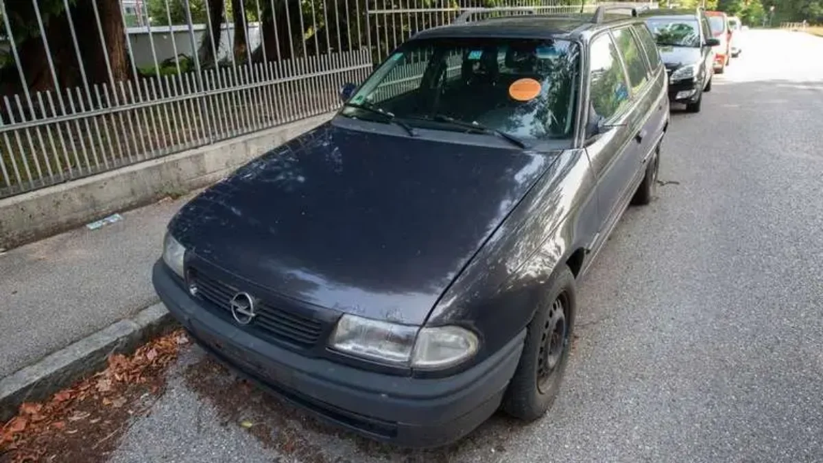 Modré auto stojí zaparkované na ulici, na čelním skle červená samolepka