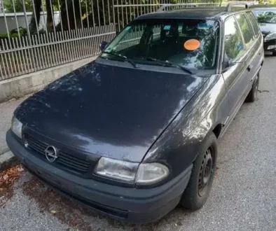 Modré auto stojí zaparkované na ulici, na čelním skle červená samolepka