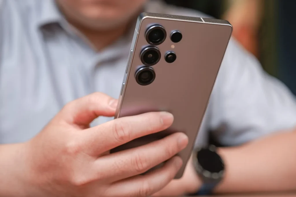 tel2 - Techsvět Muže drží moderní smartphone se čtyřmi čočkami fotoaparátu.