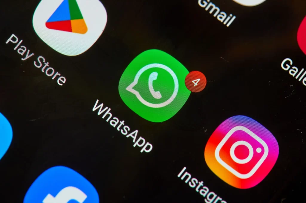 Detailní pohled na obrazovku telefonu se zobrazenými ikonami aplikací. V popředí je ikona WhatsApp s červeným oznámením o 4 nových zprávách.