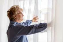 seniorka roztahuje záclony