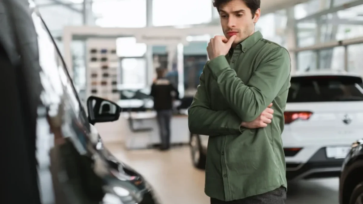 Muž v autosalonu přemýšlí nad výběrem auta