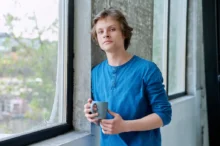 mladý kluk u okna s hrnkem kávy