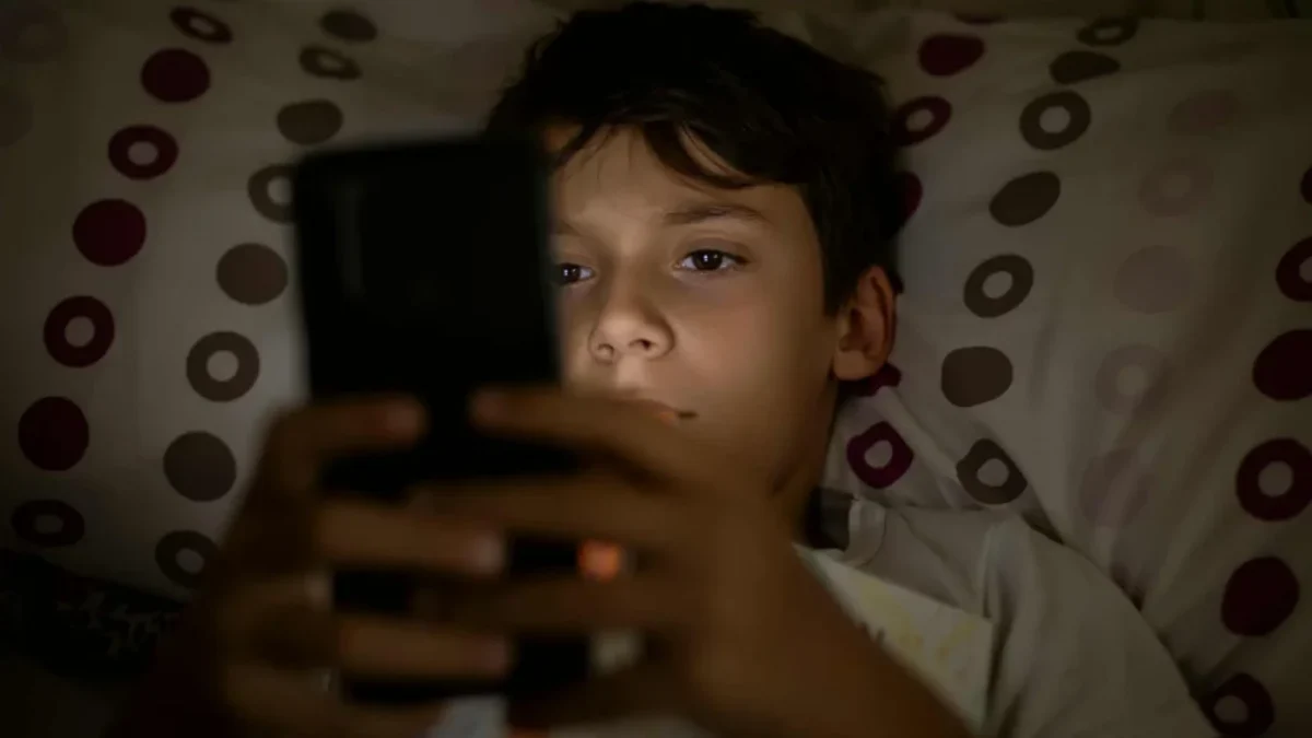 chlapec v posteli se dívá do mobilu