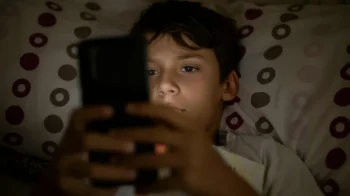 chlapec v posteli se dívá do mobilu