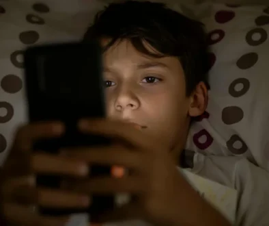 chlapec v posteli se dívá do mobilu