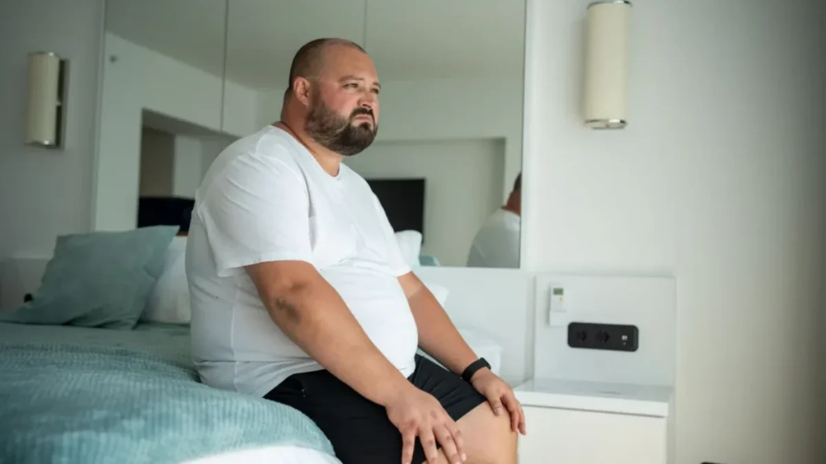 obézní muž sedí na posteli