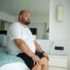 obézní muž sedí na posteli