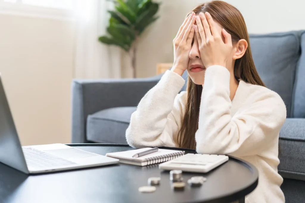 Shutterstock_2615285647 - Techsvět Nešťastná žena sedí u stolu, má před sebou pár mincí a bankovek, s výrazem zoufalství