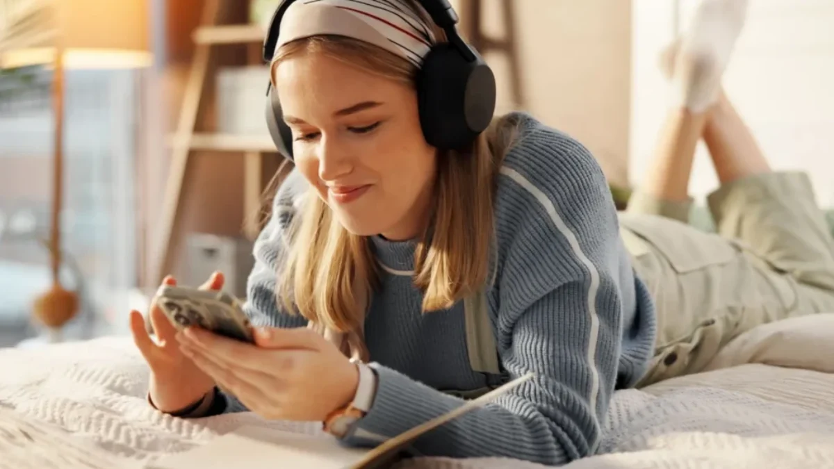 Mladá žena s mobilem a sluchátky na posteli