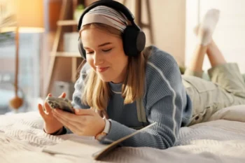 Mladá žena s mobilem a sluchátky na posteli