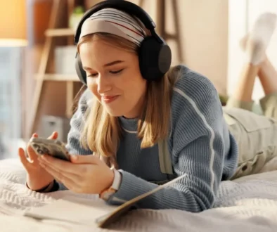 Mladá žena s mobilem a sluchátky na posteli