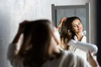 žena si suší vlasy a dívá se při tom na sebe do zrcadla