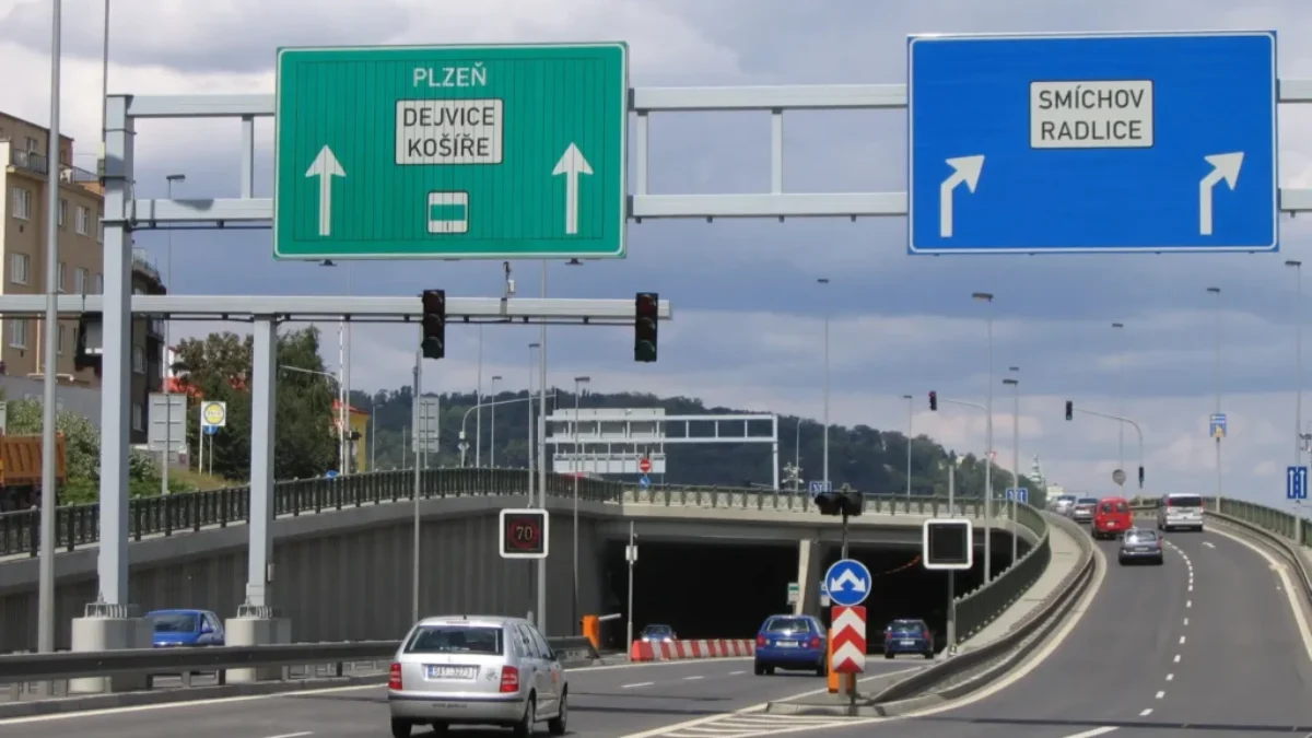 Silnice v Česku. Nalevo vede do tunelu. Napravo pokračuje nahoru. Vidět jsou auta, i značky.