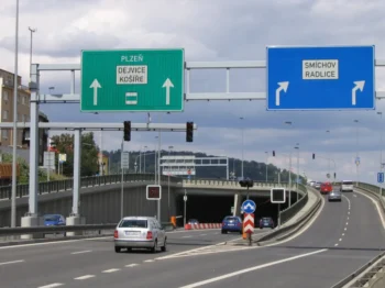 Silnice v Česku. Nalevo vede do tunelu. Napravo pokračuje nahoru. Vidět jsou auta, i značky.