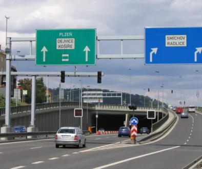 Silnice v Česku. Nalevo vede do tunelu. Napravo pokračuje nahoru. Vidět jsou auta, i značky.