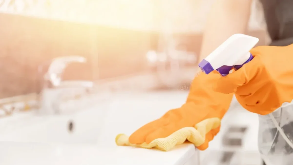 Ruce v rukavicích, houbičkou a rozprašovačem umývají umyvadlo