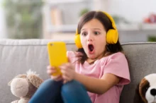 malá dívka se sluchátky a mobilem, šokovaná tím, co vidí na displeji