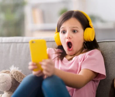 malá dívka se sluchátky a mobilem, šokovaná tím, co vidí na displeji
