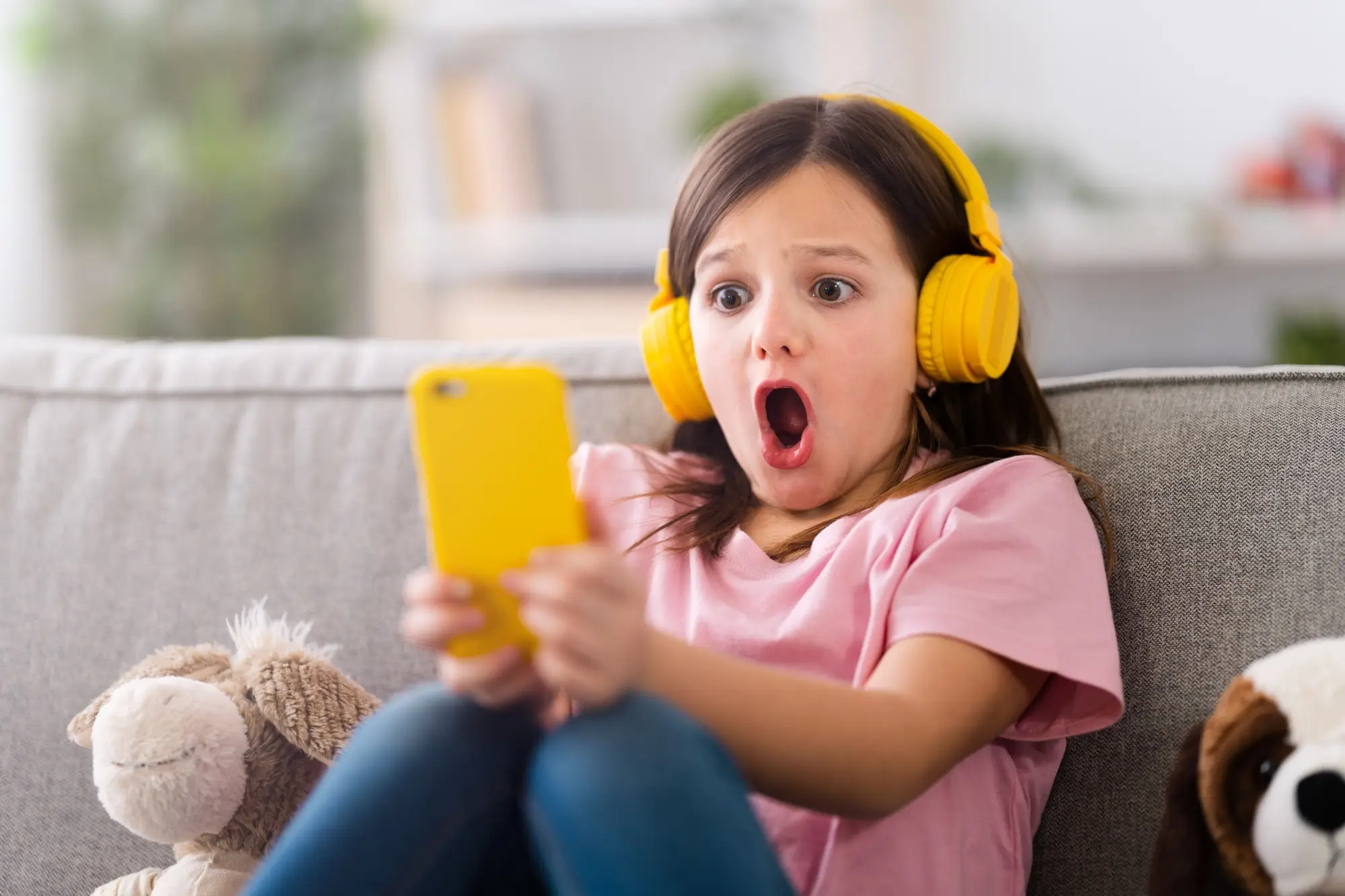 malá dívka se sluchátky a mobilem, šokovaná tím, co vidí na displeji