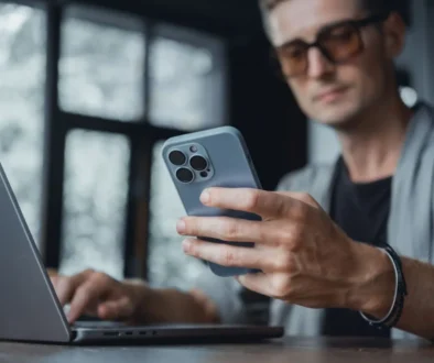 muž pracuje na laptopu a drží v ruce iPhone