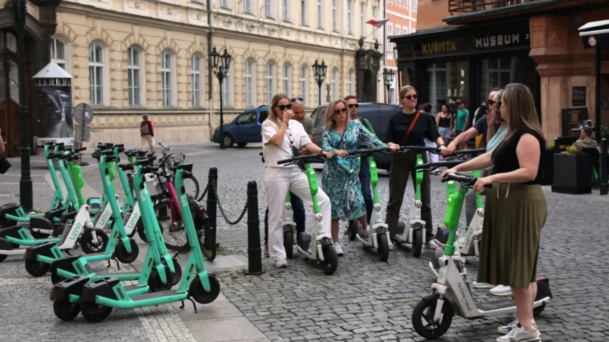 Elektrokoloběžky v pražské ulici. Stojí u nich turisté, kteří se na nich chystají odjet.