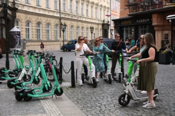 Elektrokoloběžky v pražské ulici. Stojí u nich turisté, kteří se na nich chystají odjet.