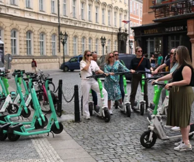 Elektrokoloběžky v pražské ulici. Stojí u nich turisté, kteří se na nich chystají odjet.