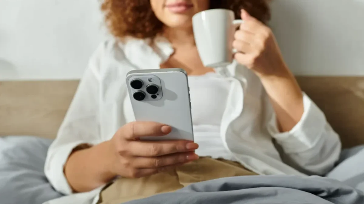 Žena s iphonem v posteli a hrnkem