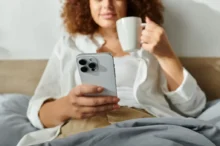 Žena s iphonem v posteli a hrnkem