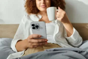 Žena s iphonem v posteli a hrnkem