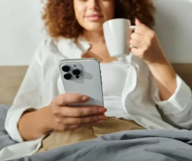 Žena s iphonem v posteli a hrnkem