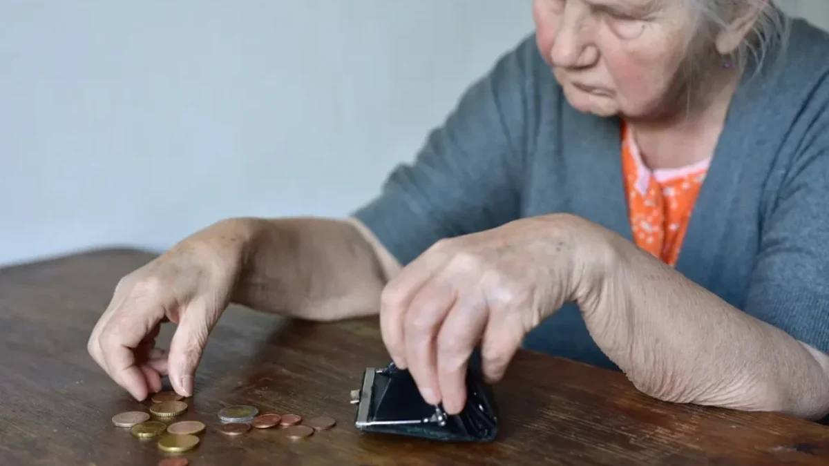 seniorka sedí u stolu a počítá drobné mince