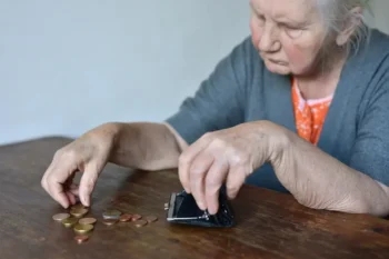 seniorka sedí u stolu a počítá drobné mince