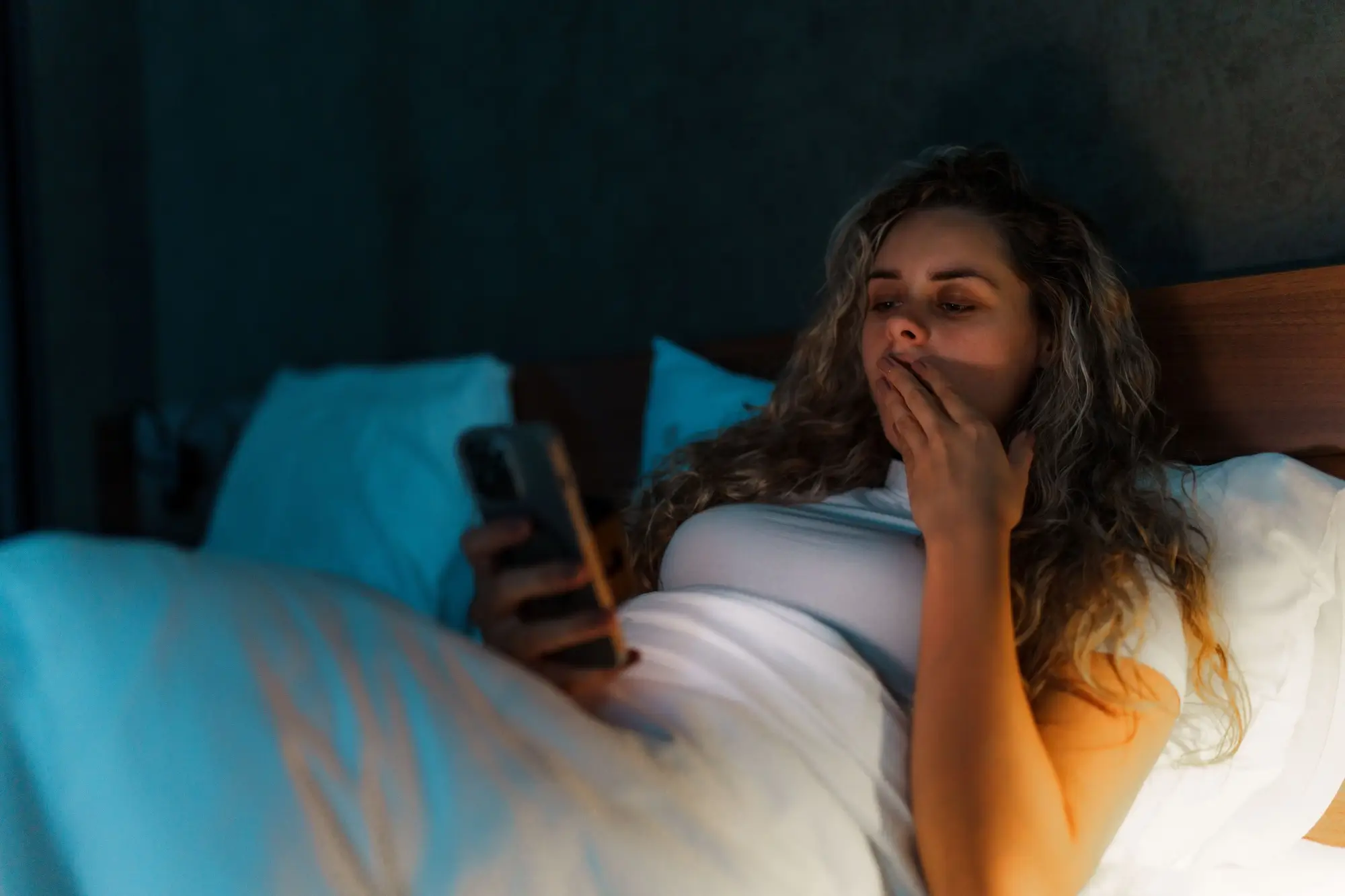 Žena se dívá v posteli na telefon