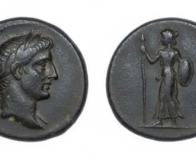Ancient coin with a left-facing male head (obverse) and a standing female figure with spear and shield (reverse); scale shows 1 mm.