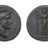 Ancient coin with a left-facing male head (obverse) and a standing female figure with spear and shield (reverse); scale shows 1 mm.
