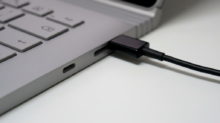 Close-up of a laptop with a black cable plugged into a side port on its silver chassis.