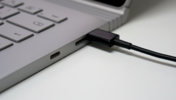 Close-up of a laptop with a black cable plugged into a side port on its silver chassis.