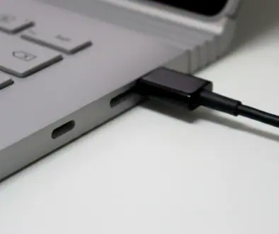 Close-up of a laptop with a black cable plugged into a side port on its silver chassis.