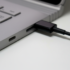 Close-up of a laptop with a black cable plugged into a side port on its silver chassis.