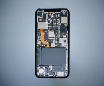Close-up of a smartphone with its back removed, exposing motherboard, circuits, and orange flex cable along the side.