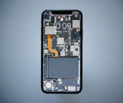 Close-up of a smartphone with its back removed, exposing motherboard, circuits, and orange flex cable along the side.