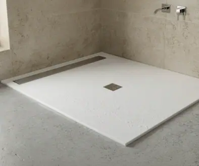 White rectangular shower base with a square drain in a minimalist bathroom, beige tiled walls, and wall-mounted faucets to the right.