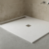 White rectangular shower base with a square drain in a minimalist bathroom, beige tiled walls, and wall-mounted faucets to the right.