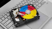 Hard disk drive resting on a silver laptop keyboard with a multicolored, Google-style circular label on the platter.