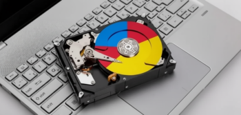 Hard disk drive resting on a silver laptop keyboard with a multicolored, Google-style circular label on the platter.