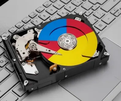 Hard disk drive resting on a silver laptop keyboard with a multicolored, Google-style circular label on the platter.